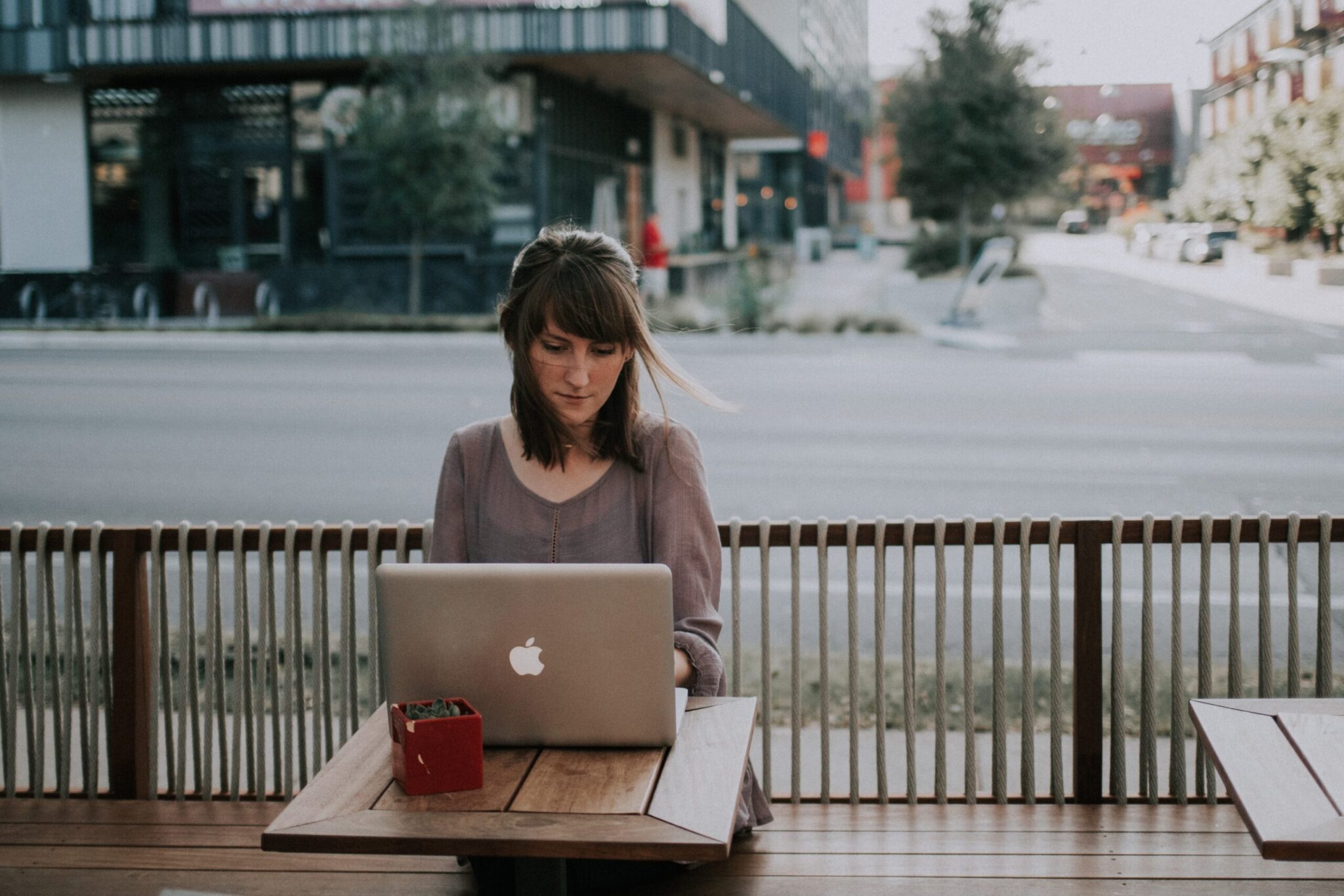 Woman with brown hair writing blogging tips article on laptop sitting outside at restaurant